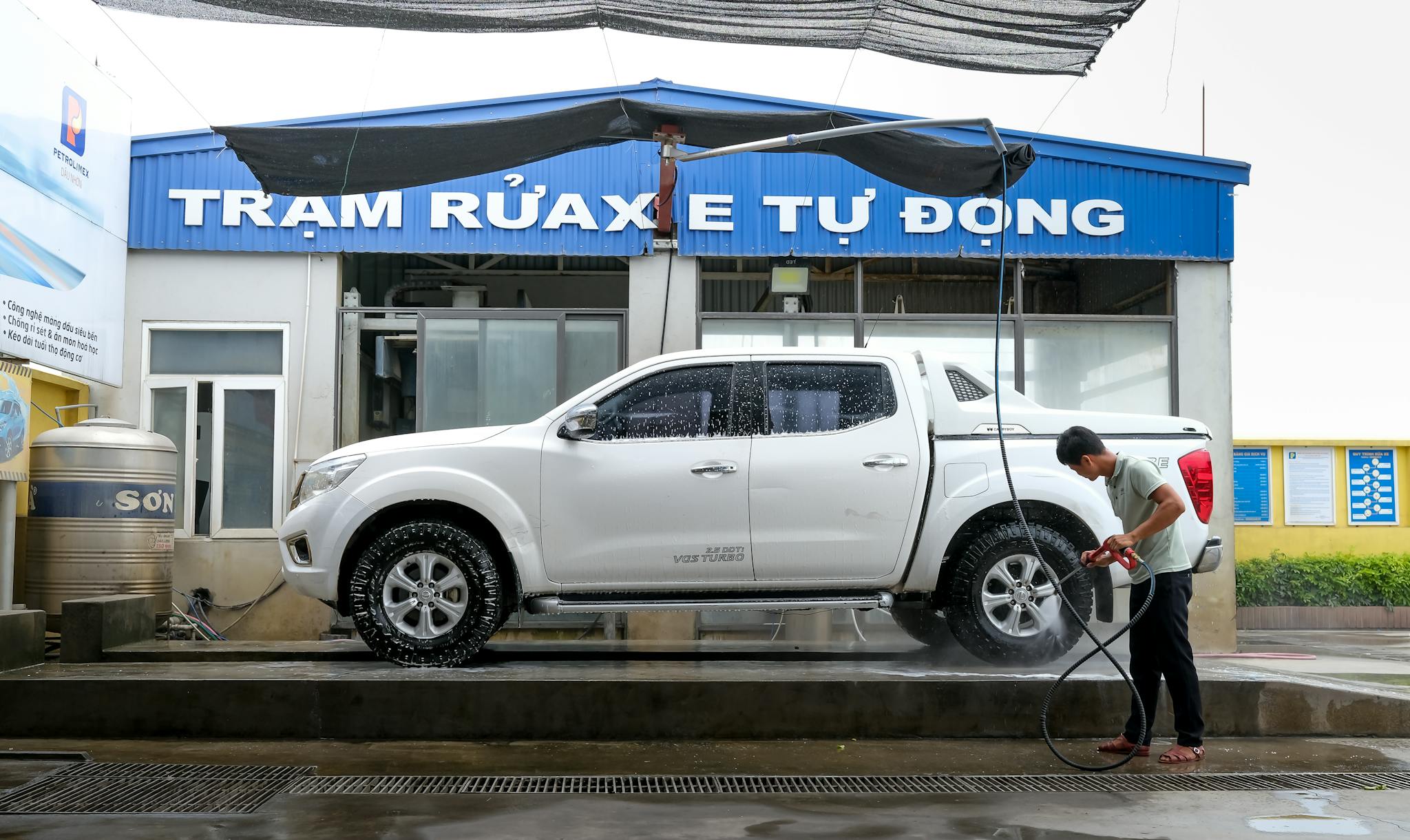 Man cleaning white pickup truck at automated car wash with pressure washer.